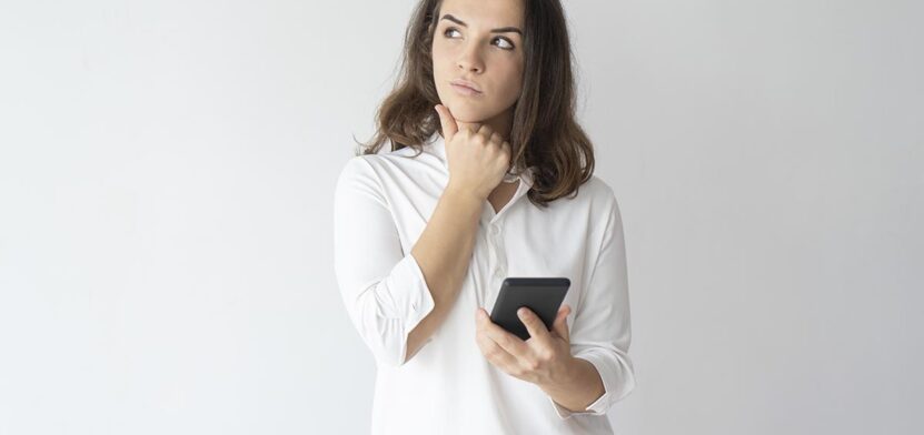 Pensive girl thinking over text message. Young Caucasian woman holding smartphone, leaning chin on hand and looking away. Reflecting and communication concept